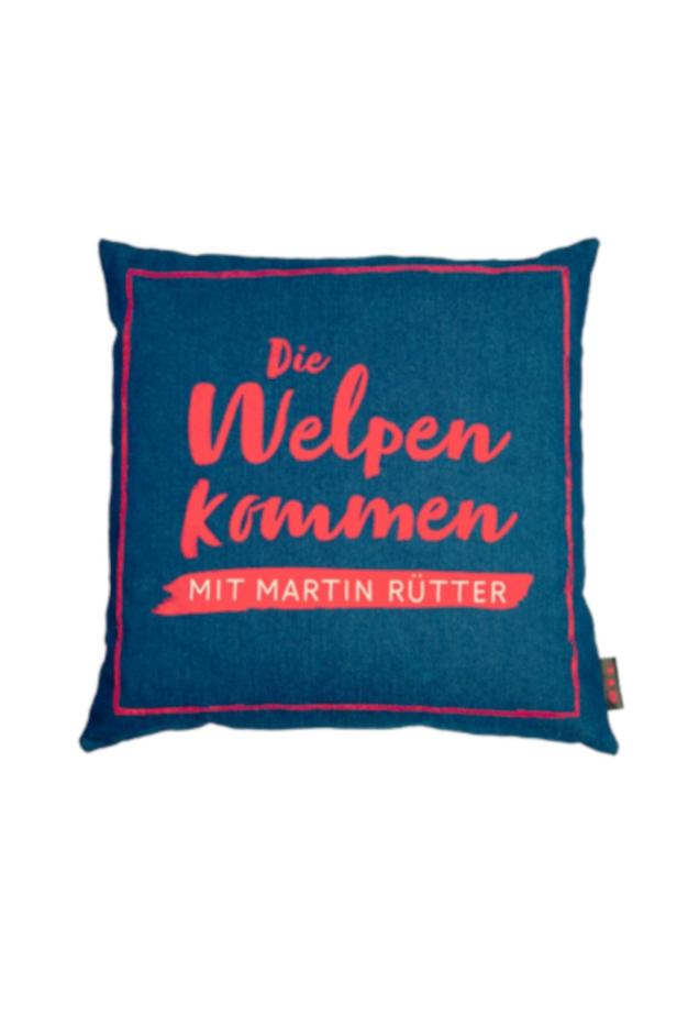 Ein blaues Kissen mit der Aufschrift „Die Welpen kommen – Mit Martin Rütter“.