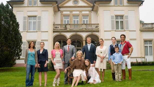 Eine Gruppe von Menschen posiert vor einem großen, herrschaftlichen Haus.