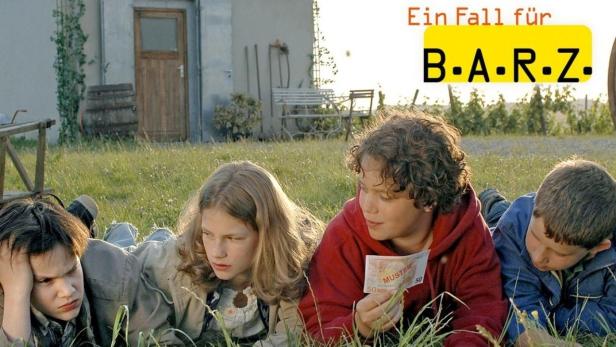 Vier Kinder liegen im Gras, im Hintergrund der Schriftzug „Ein Fall für B.A.R.Z.“.