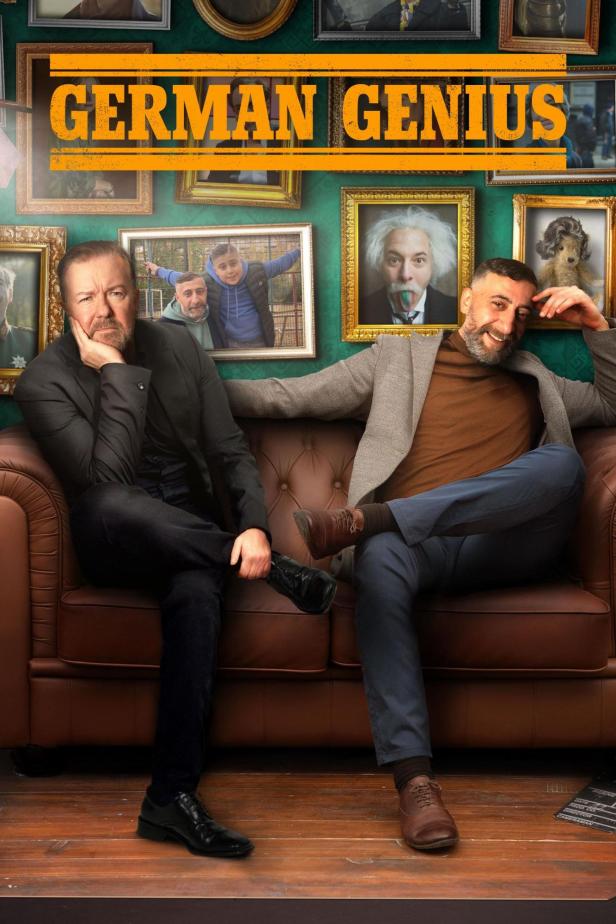 Ricky Gervais und Christoph Maria Herbst sitzen auf einer Couch vor einer Wand mit gerahmten Bildern für „German Genius“.
