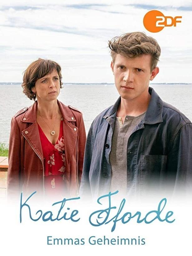 Das Filmplakat zu „Katie Fforde: Emmas Geheimnis“ zeigt eine Frau und einen Mann vor einer Küstenlandschaft.