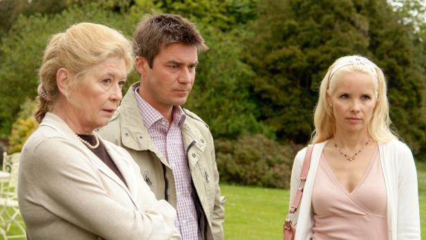 Drei Personen stehen im Freien vor einem grünen Hintergrund.