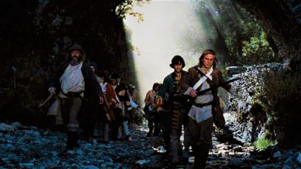 Eine Gruppe von Männern in historischer Kleidung wandert durch einen Wald.