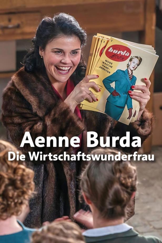 Eine lächelnde Frau im Pelzmantel hält mehrere Ausgaben der „Burda Moden“ hoch.
