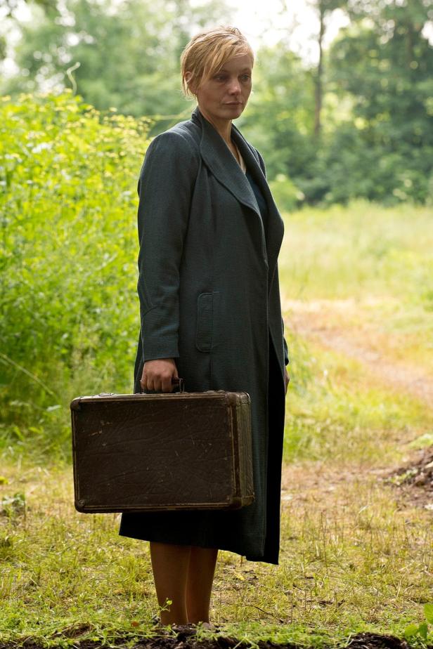 Eine Frau mit einem alten Koffer steht auf einer Wiese.