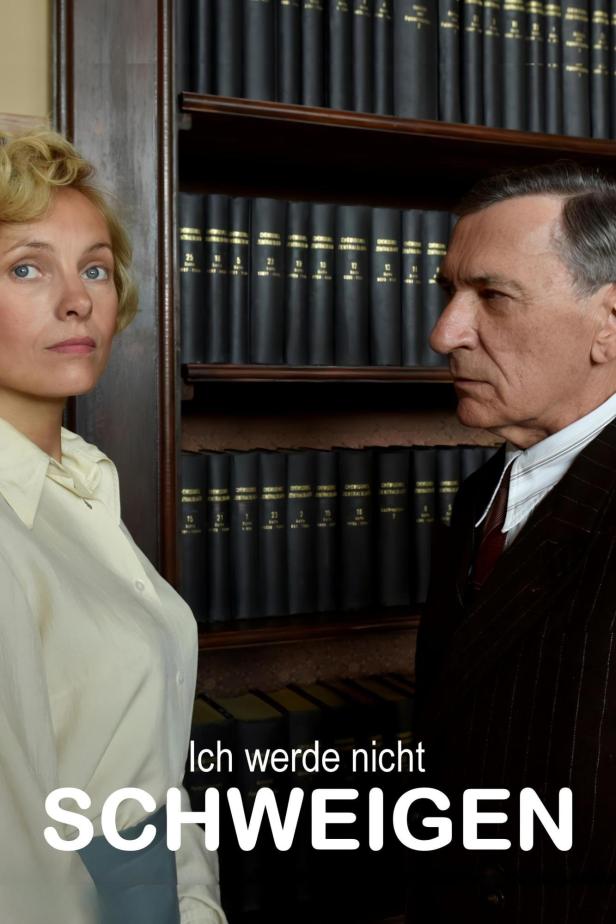 Eine Frau und ein Mann stehen vor einem Bücherregal; Filmposter „Ich werde nicht schweigen“.