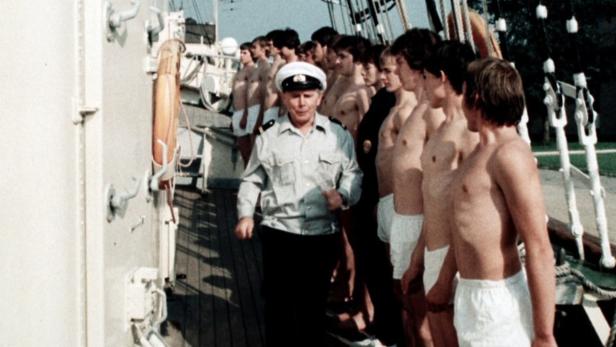 Ein Marineoffizier inspiziert eine Reihe junger Männer an Deck eines Schiffes.