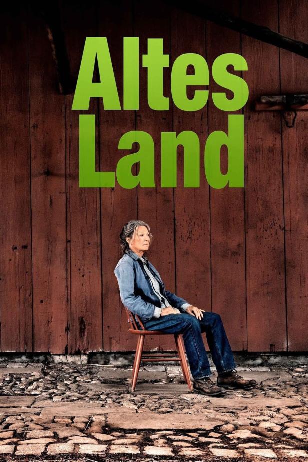 Eine Frau sitzt vor einer Holzwand unter dem grünen Schriftzug „Altes Land“.