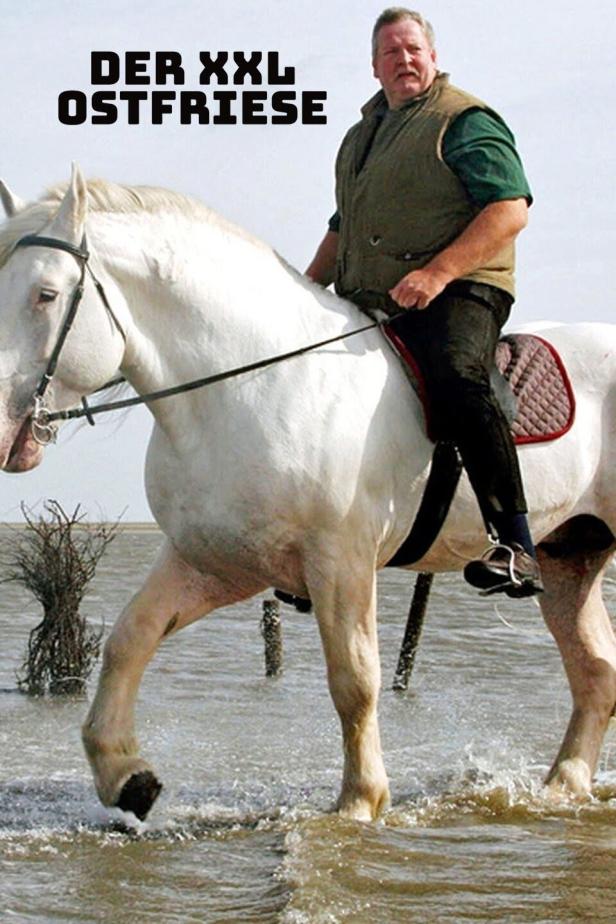 Ein Mann reitet auf einem weißen Pferd durch das flache Wasser.