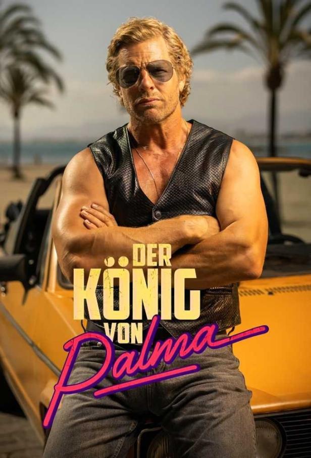 Ein Mann mit Sonnenbrille posiert vor dem Schriftzug „Der König von Palma“ und einem gelben Auto.