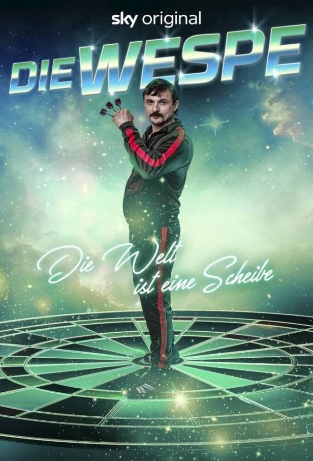 Ein Mann im Trainingsanzug steht auf einer Dartscheibe und hält Darts in der Hand, im Hintergrund das Logo von „Die Wespe“.