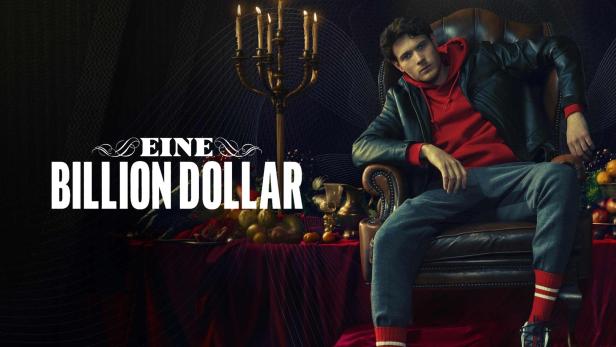 Ein Mann sitzt lässig in einem Ledersessel vor einem Tisch mit Kerzenleuchter und Früchten.