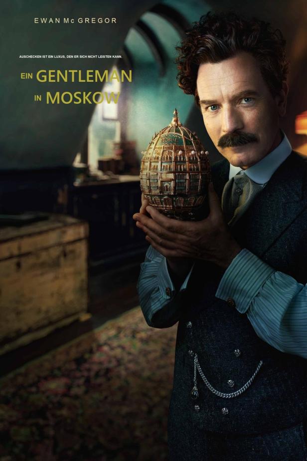 Ewan McGregor hält ein Miniaturmodell des Hotels Metropol in den Händen, wie auf dem Poster zu „Ein Gentleman in Moskau“.