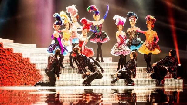 Eine Gruppe von Tänzerinnen in farbenprächtigen Kostümen und Kopfbedeckungen auf einer Bühne.