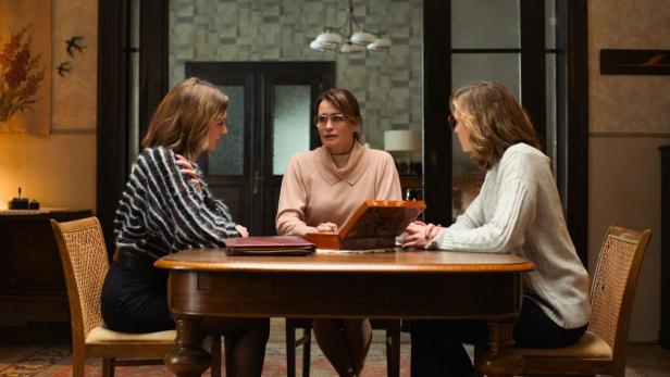 Drei Frauen sitzen an einem Tisch in einem Wohnzimmer und unterhalten sich.