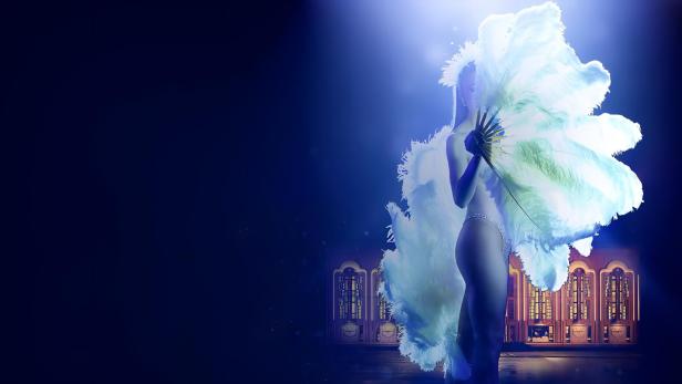 Eine Frau in einem Federkostüm hält einen Fächer vor einem dunklen Bühnenhintergrund.