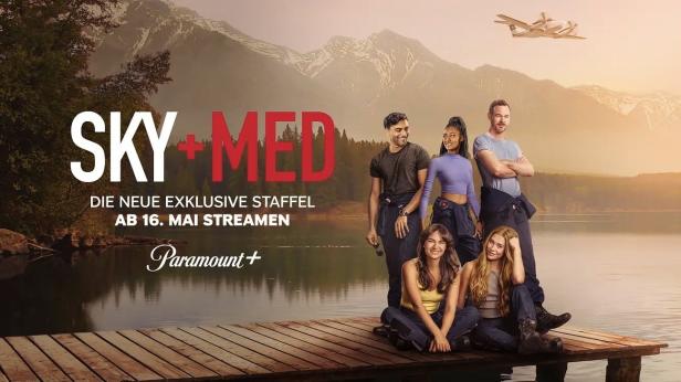 Die Besetzung von „SkyMed“ posiert vor einem Bergsee mit einem Wasserflugzeug in der Luft.