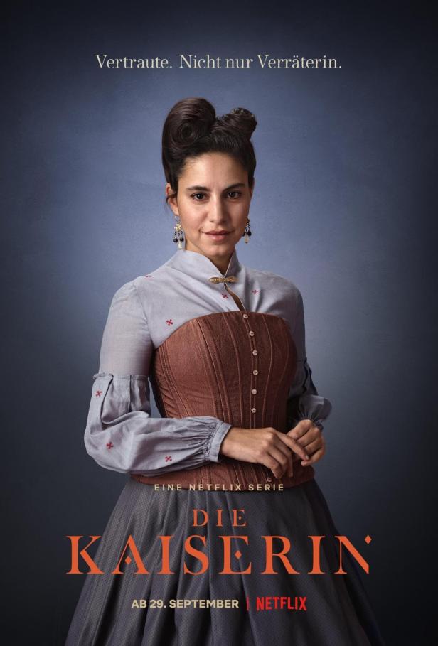Porträt einer Frau im Kostüm vor dem Hintergrund des Posters für die Netflix-Serie „Die Kaiserin“.