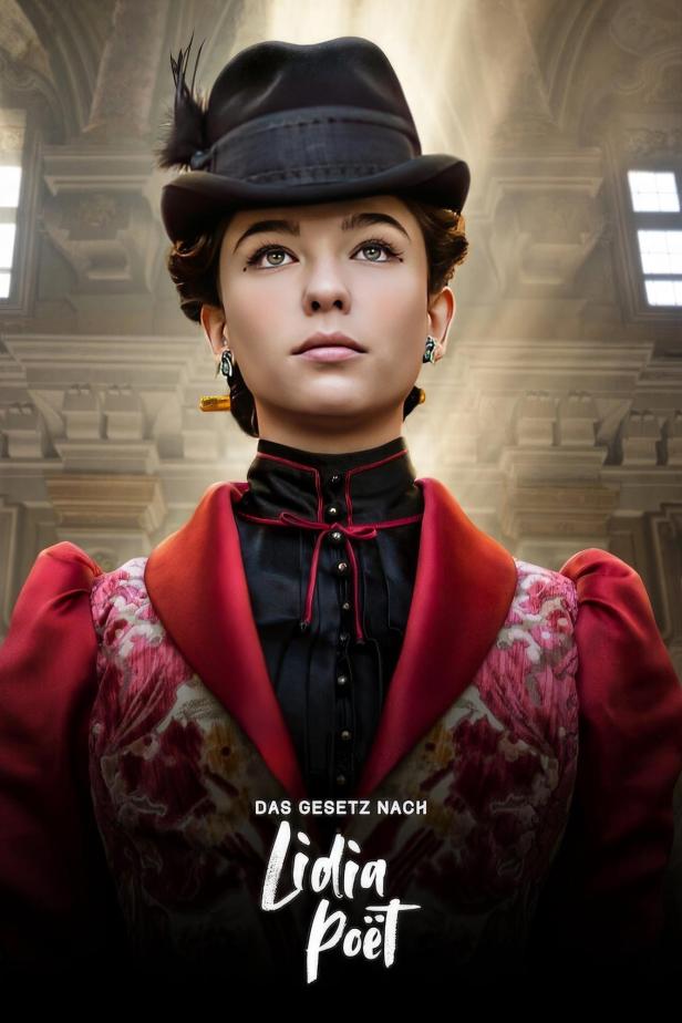 Eine junge Frau mit Hut und rotem Kleid, im Hintergrund ein Gebäude, vermutlich ein Filmposter für „Lidia Poët“.