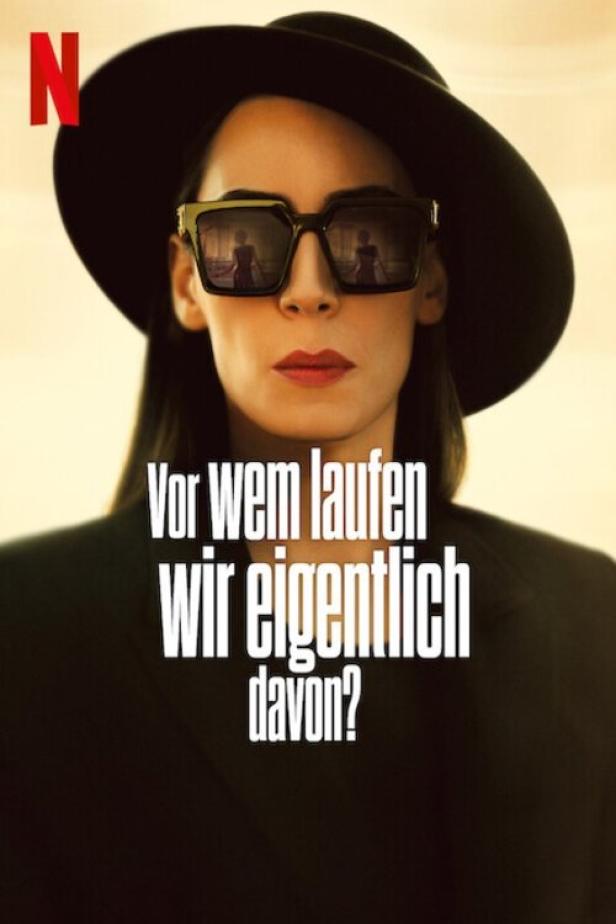 Eine Frau mit Hut und Sonnenbrille, auf deren Gläsern sich ein Spiegelbild befindet.