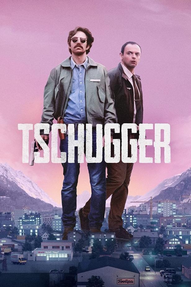 Das Filmplakat zu „Tschugger“ zeigt zwei Männer vor einer Stadtkulisse und Bergen.
