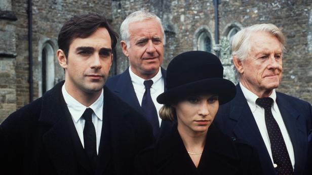 Vier Personen in formeller Kleidung stehen vor einem Gebäude.