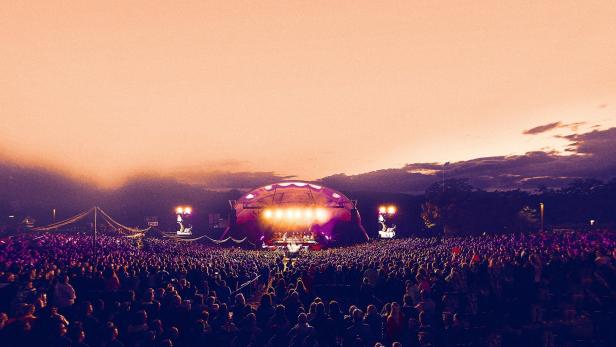 Eine große Menschenmenge versammelt sich vor einer beleuchteten Bühne bei einem Open-Air-Konzert.