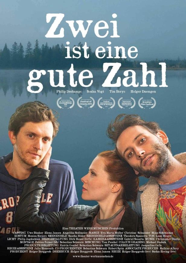 Das Filmplakat zu „Zwei ist eine gute Zahl“ zeigt drei Schauspieler vor einem See.