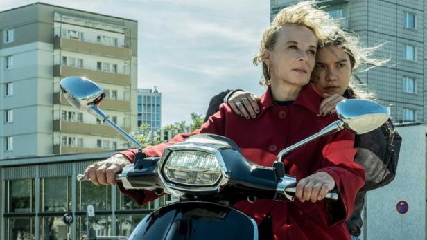 Eine Frau und ein Mädchen fahren zusammen auf einem Motorroller durch die Stadt.