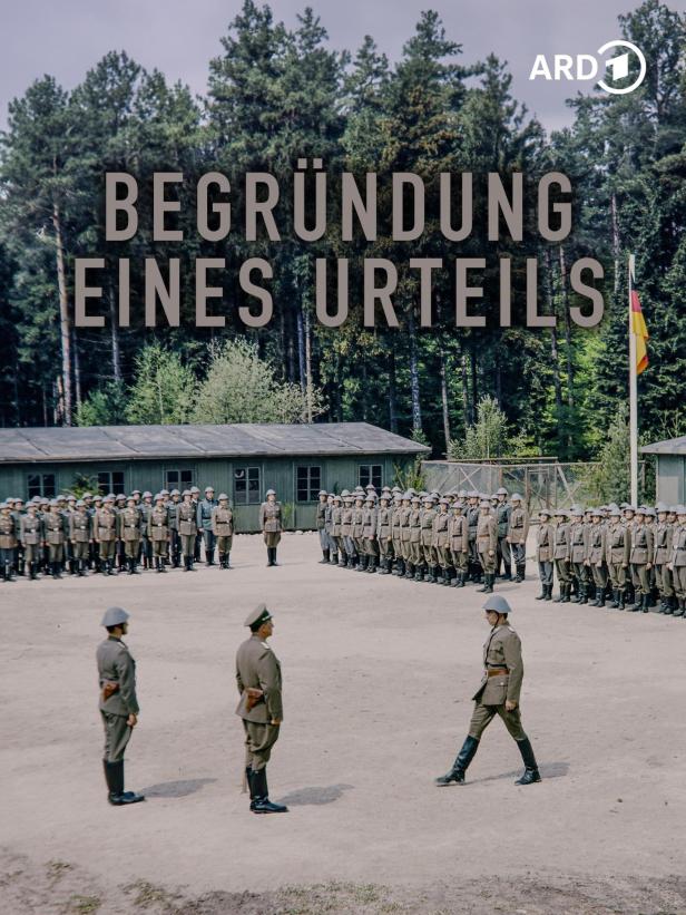 Soldaten in Uniform stehen auf einem Exerzierplatz vor Baracken und einer Deutschlandflagge.