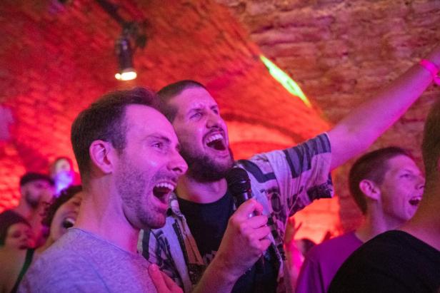Zwei Männer singen in ein Mikrofon auf einer Party oder in einer Bar.