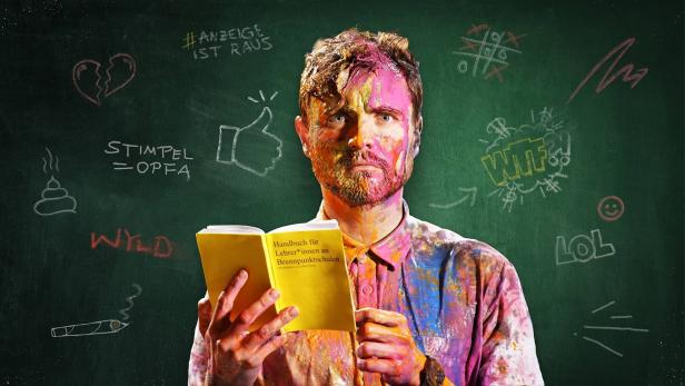 Ein mit Farbe beschmierter Mann liest ein „Handbuch für Lehrer*innen an Brennpunktschulen“ vor einer Tafel mit Kritzeleien.