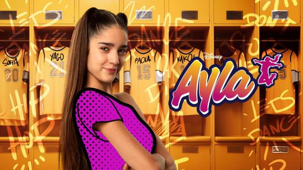 Eine junge Frau vor gelben Spinden mit Trikots und dem Schriftzug „Ayla“.