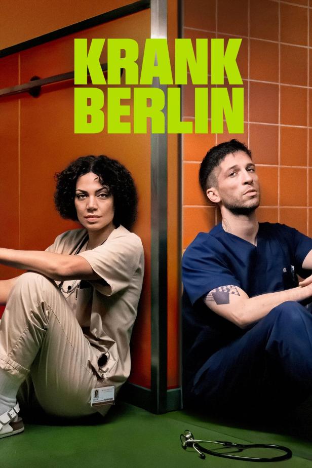 Zwei erschöpfte Pflegekräfte sitzen vor orangefarbenen Fliesen, darüber der Titel „Krank Berlin“.