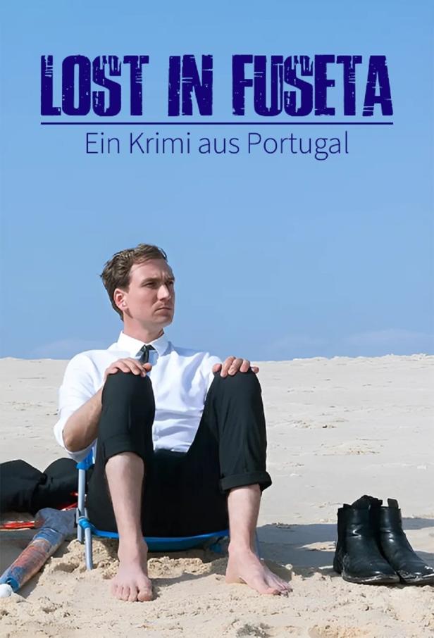 Ein Mann im Anzug sitzt barfuß am Strand, im Hintergrund das Filmplakat „Lost in Fuseta“.