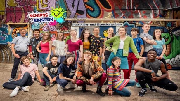Eine Gruppe Jugendlicher steht vor einer mit Graffiti bemalten Wand mit dem „Schloss Einstein“-Logo.
