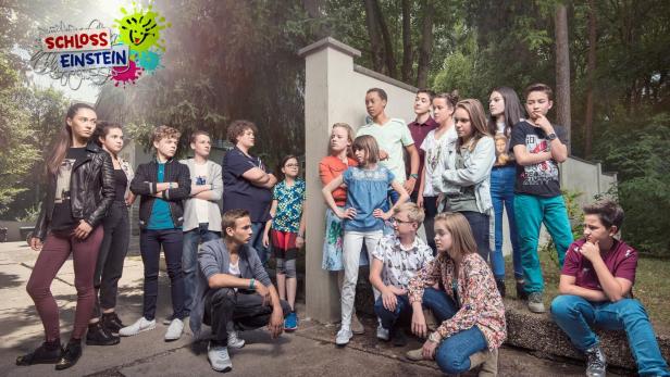 Eine Gruppe Jugendlicher steht vor dem Logo der Fernsehserie „Schloss Einstein“.
