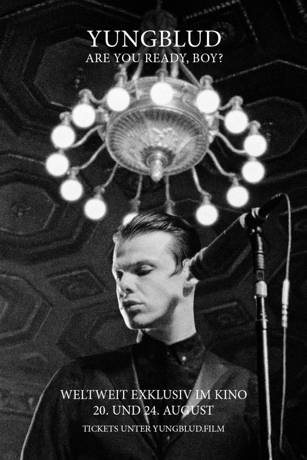 Ein Schwarzweißfoto von YUNGBLUD vor einem Mikrofon und einem Kronleuchter.