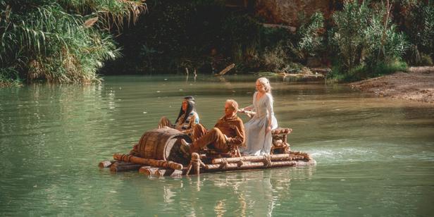Zwei Männer und eine Frau fahren auf einem Floß einen Fluss entlang, möglicherweise aus dem Film „Der Schuh des Manitu“.