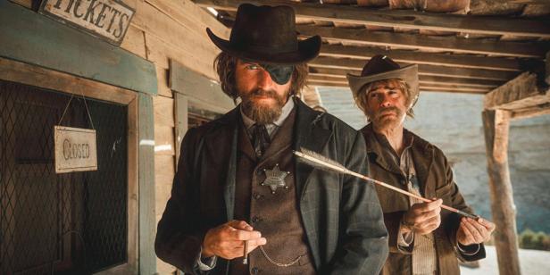 Ein Sheriff mit Augenklappe und Pfeil in der Brust steht vor einem geschlossenen Ticketschalter.