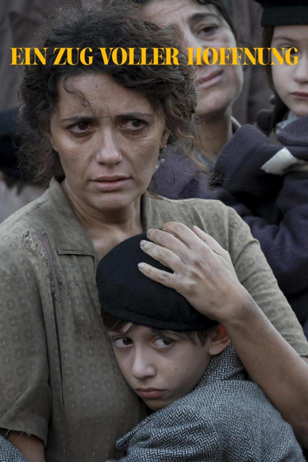 Eine besorgte Mutter umarmt ihren Sohn; im Hintergrund weitere Menschen.