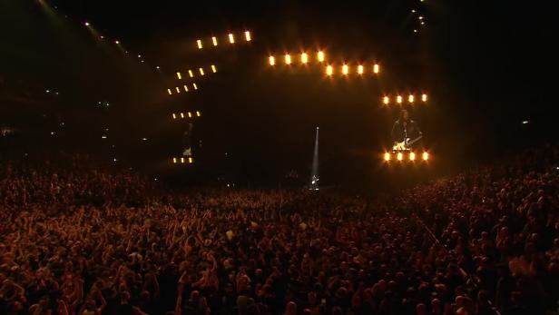 Ein Konzert mit einer Band auf der Bühne vor einem großen Publikum.