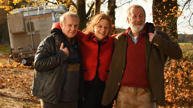 Drei Personen stehen im Herbst vor einem Wohnwagen und lächeln.