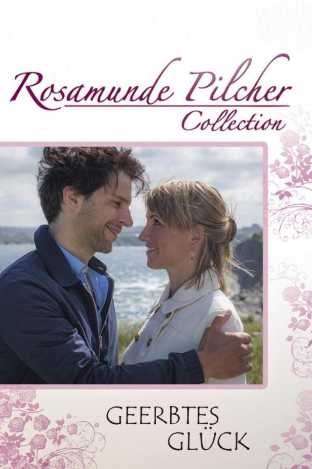 Ein lächelndes Paar steht vor dem Meer, Szene aus „Geerbtes Glück“ von Rosamunde Pilcher.