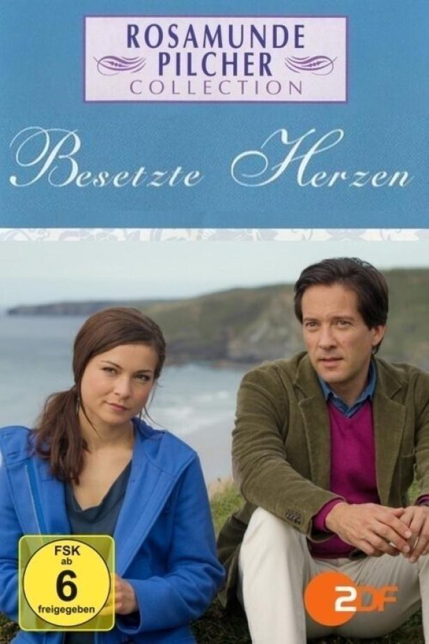 Das Cover des Films „Besetzte Herzen“ aus der Rosamunde Pilcher Collection mit zwei Schauspielern vor einer Küstenlandschaft.