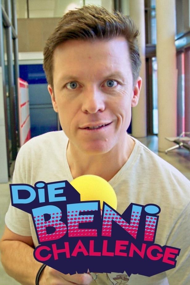 Ein Mann lächelt in die Kamera und hält ein Mikrofon mit dem Schriftzug „Die Beni Challenge“.