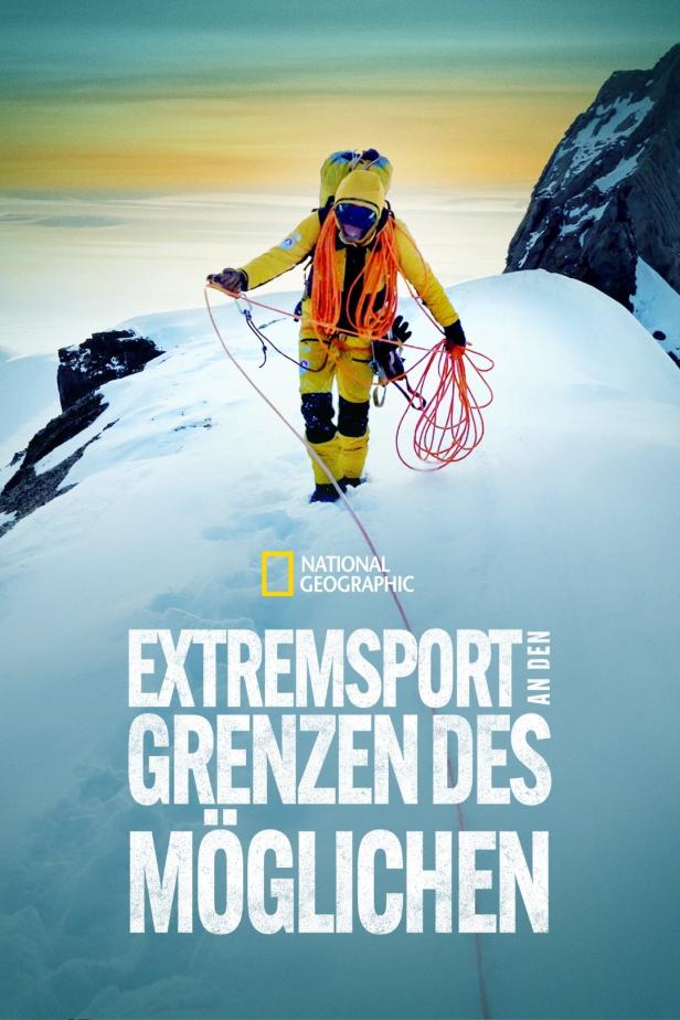 Ein Bergsteiger in gelber Kleidung steht auf einem schneebedeckten Gipfel mit Seilen.