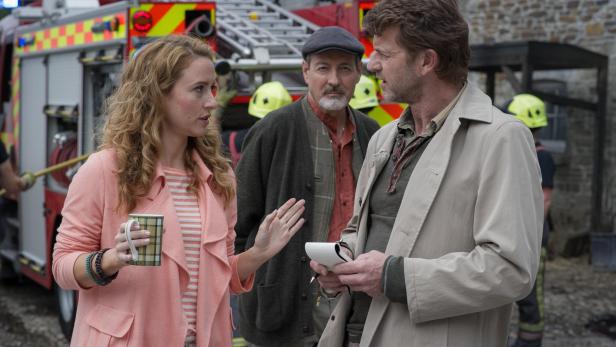 Eine Frau mit einer Tasse spricht mit einem Mann vor einem Feuerwehrauto.
