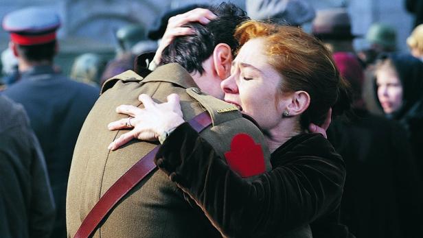 Eine Frau umarmt einen Soldaten in Uniform vor einer Menschenmenge.