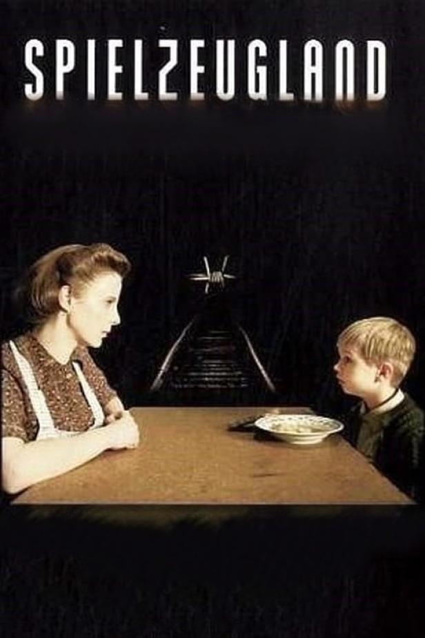 Eine Frau und ein Kind sitzen an einem Tisch vor einem Gleis und Stacheldraht, im Hintergrund der Titel „Spielzeugland“.